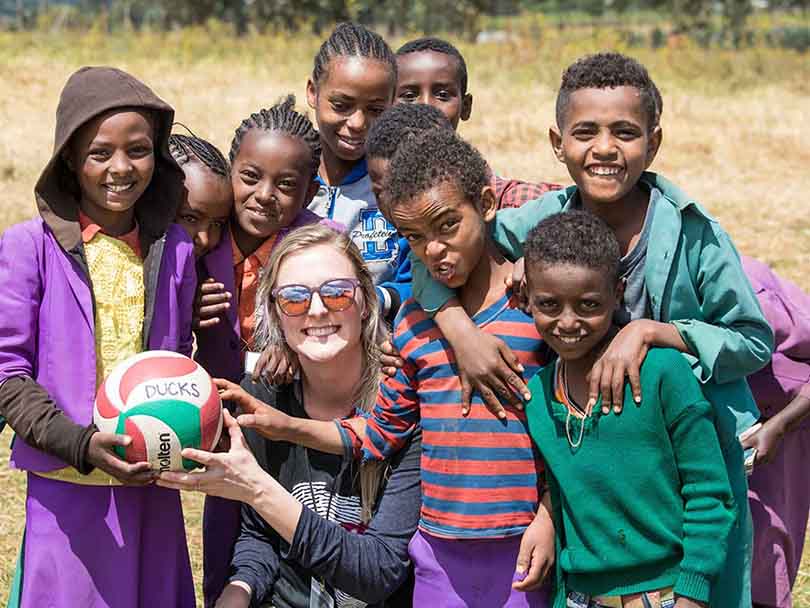 American woman and group of African kids smiling while holding a football, posing for a picture