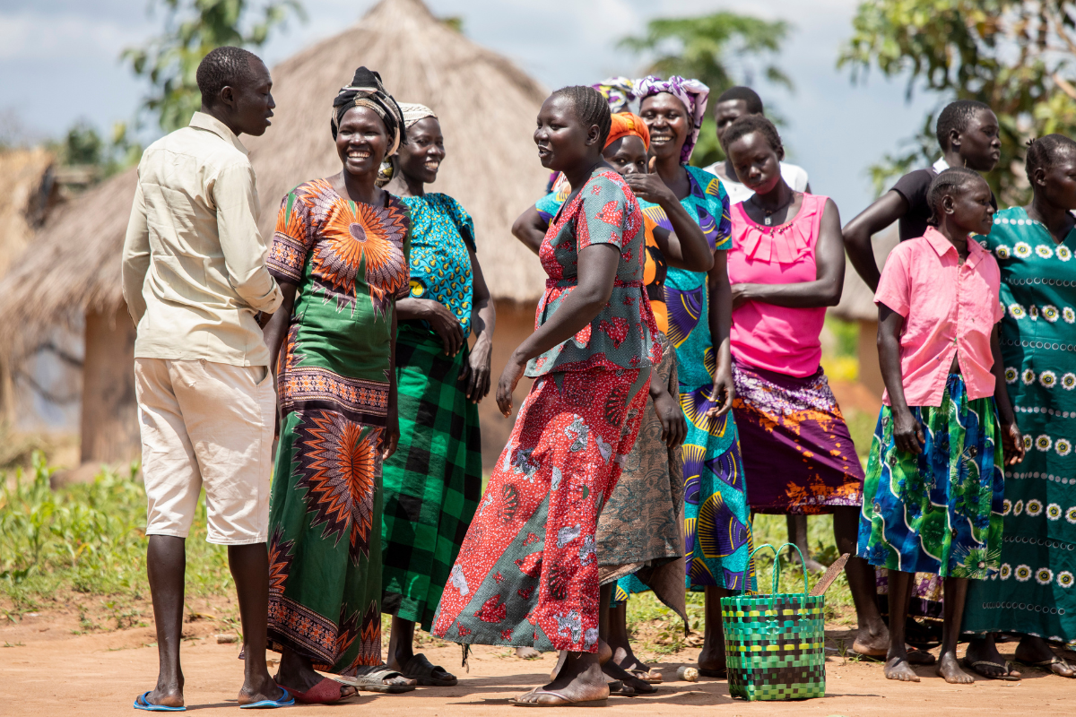 Community members standing around smiling in South Sudan wearing bright colored traditional dress.