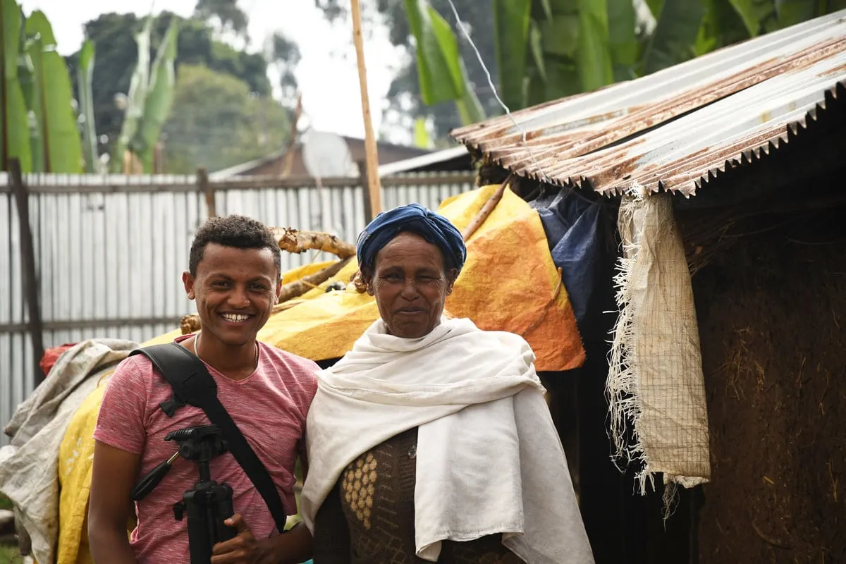 Negase standing next to a young man, smiling, in front of her home