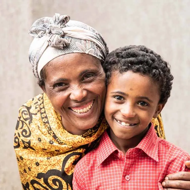 A woman is standing with his son, and both are smiling towards the camera