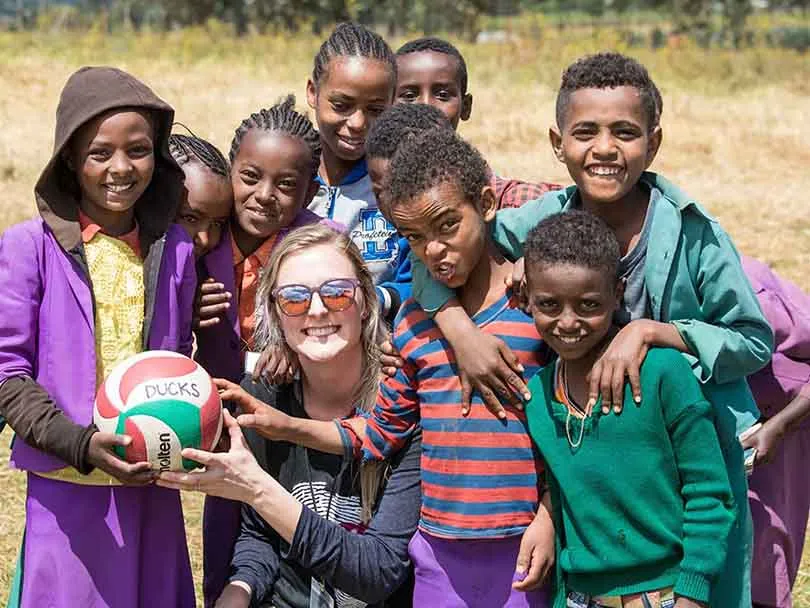 American woman and group of African kids smiling while holding a football, posing for a picture