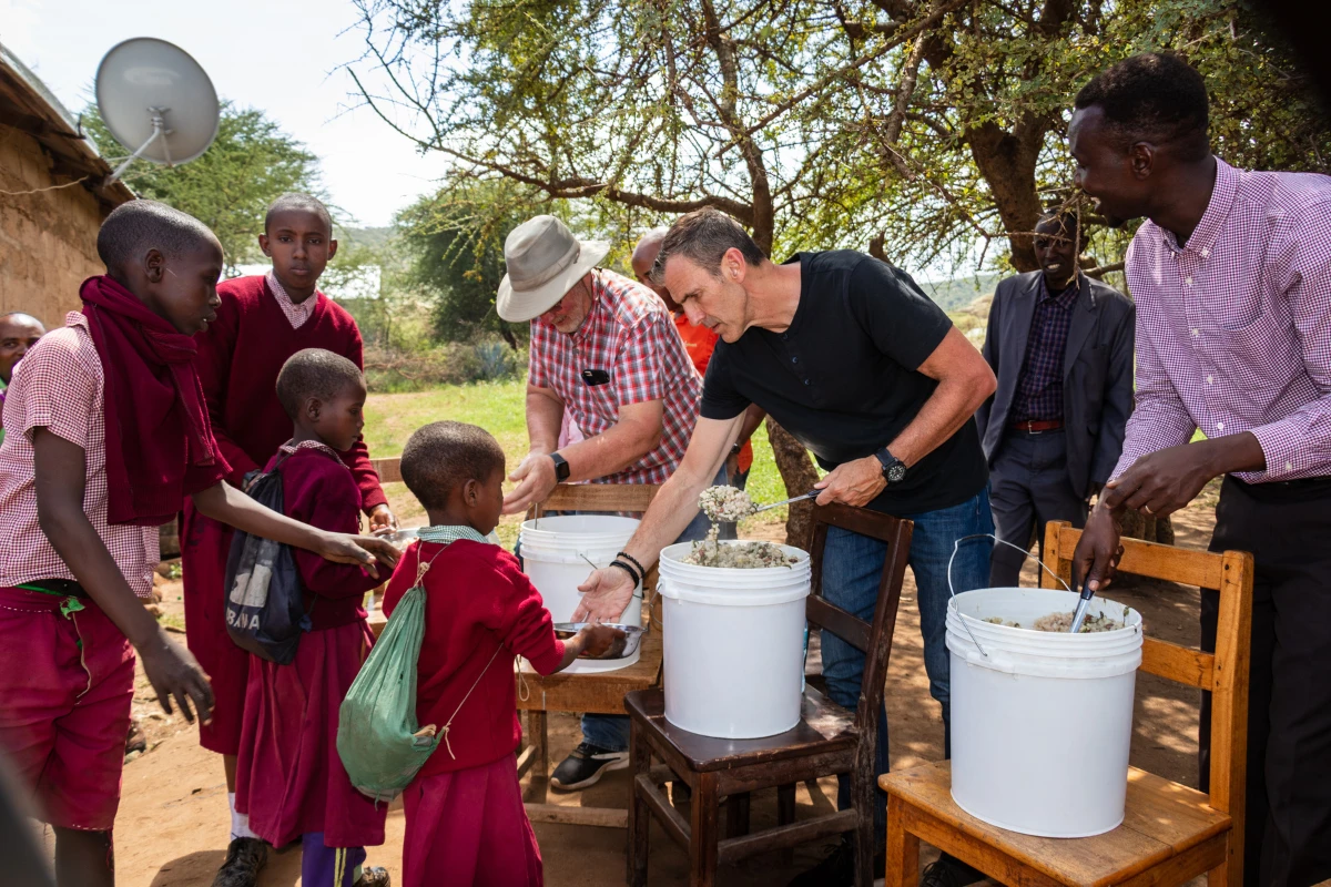 Men distributing food to children in school uniforms
