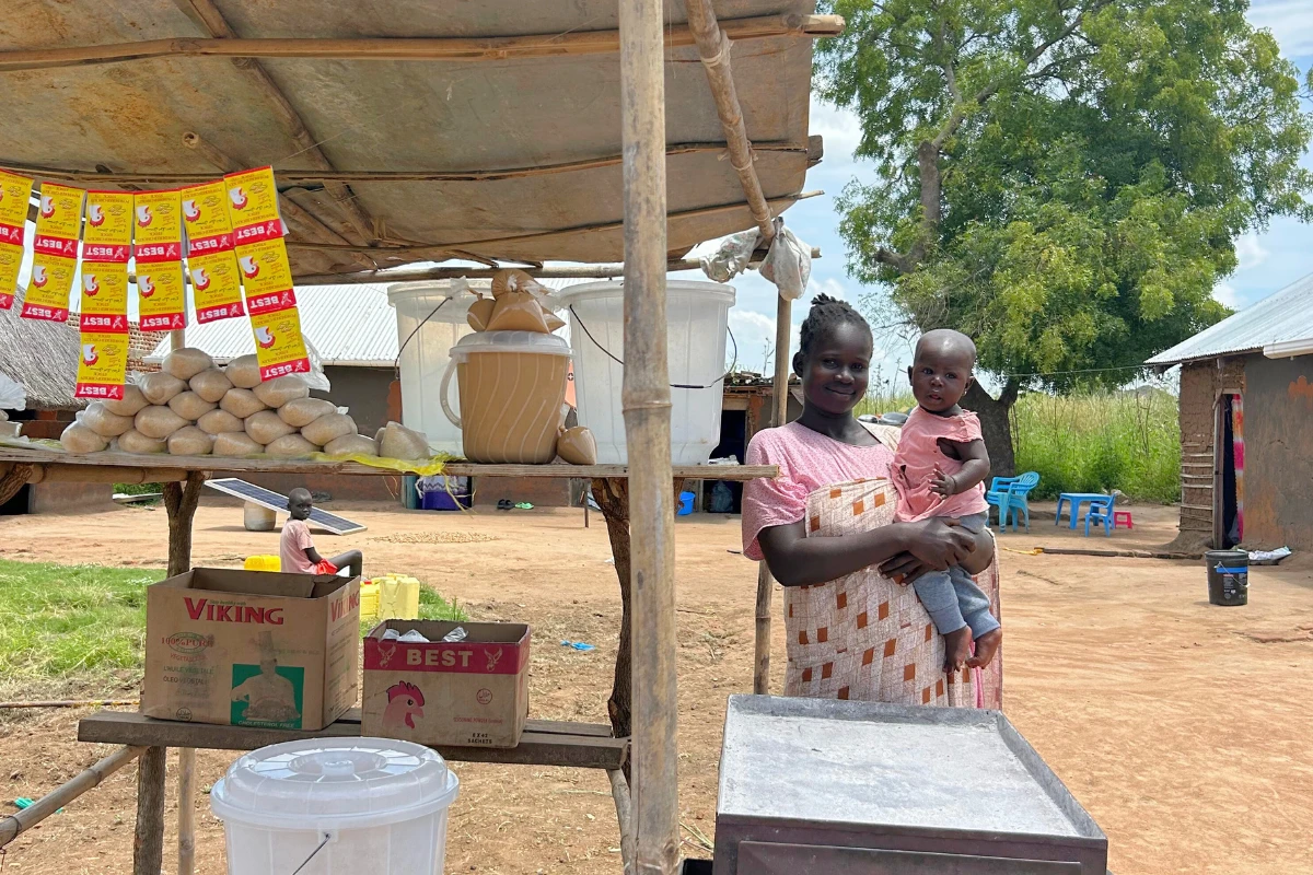 Rabba stands at her bread stand in Morwari, South Sudan, holding her six-month-old baby. Her bread is nearly sold out for the day.