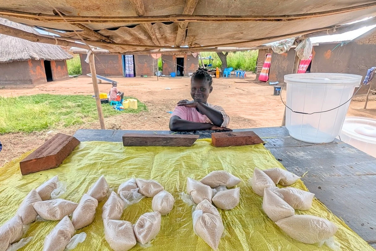 Rabba behind her market table in Morwari, South Sudan — bags of salt arranged in front of her, spelling a single word: HOPE.